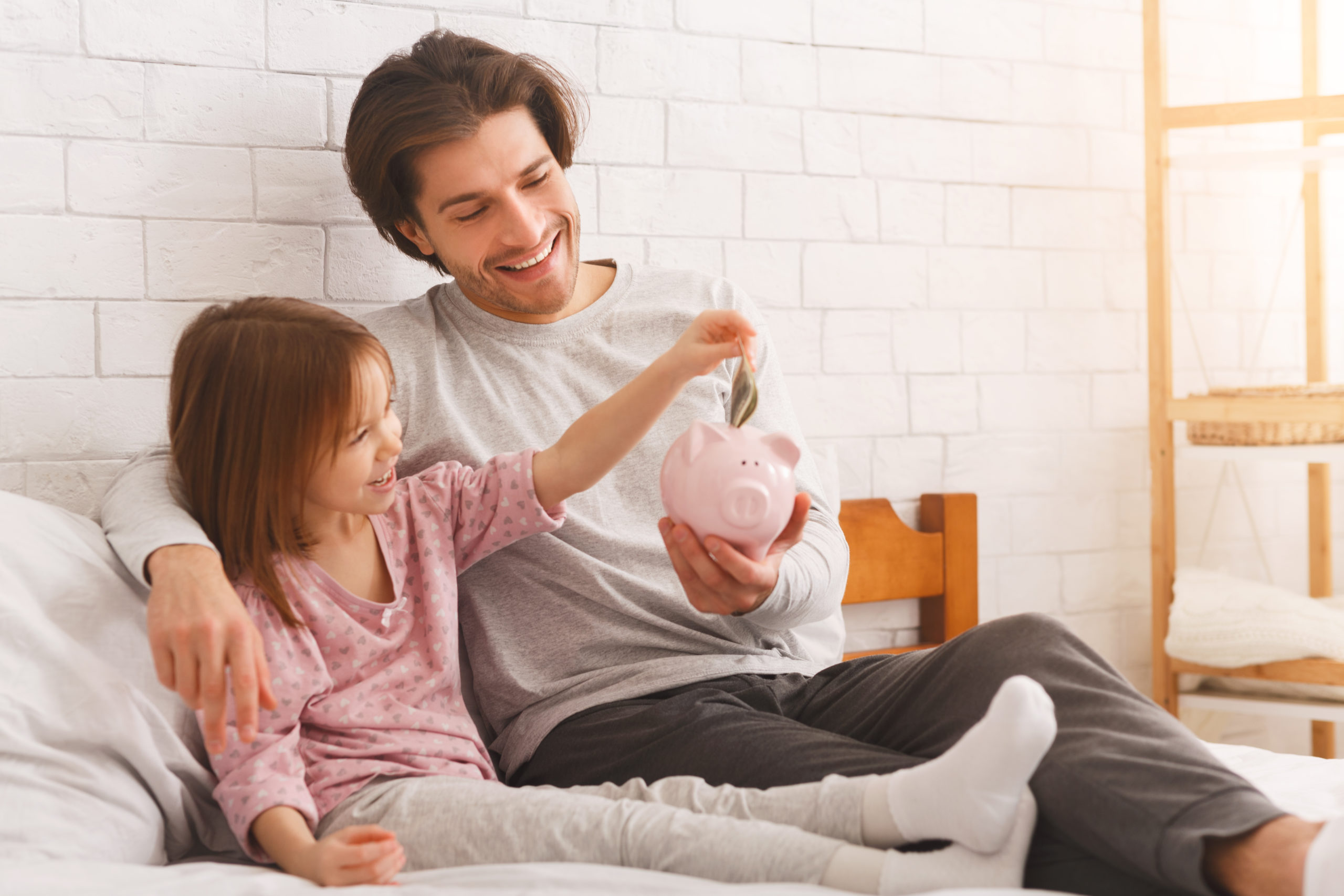 father teaching little daughter to save money in piggy bank