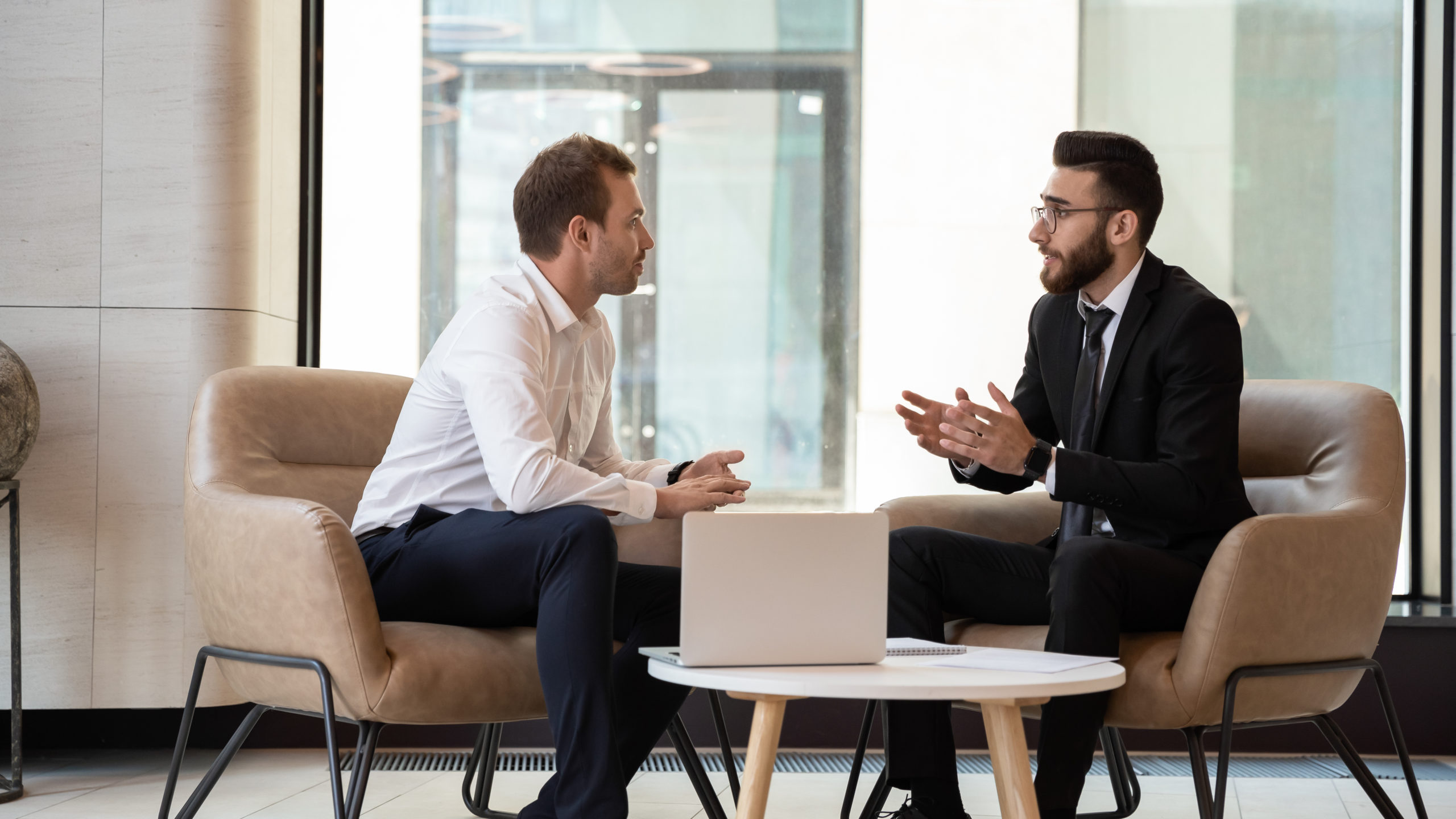 middle eastern and caucasian ethnicity businessmen seated on armchair