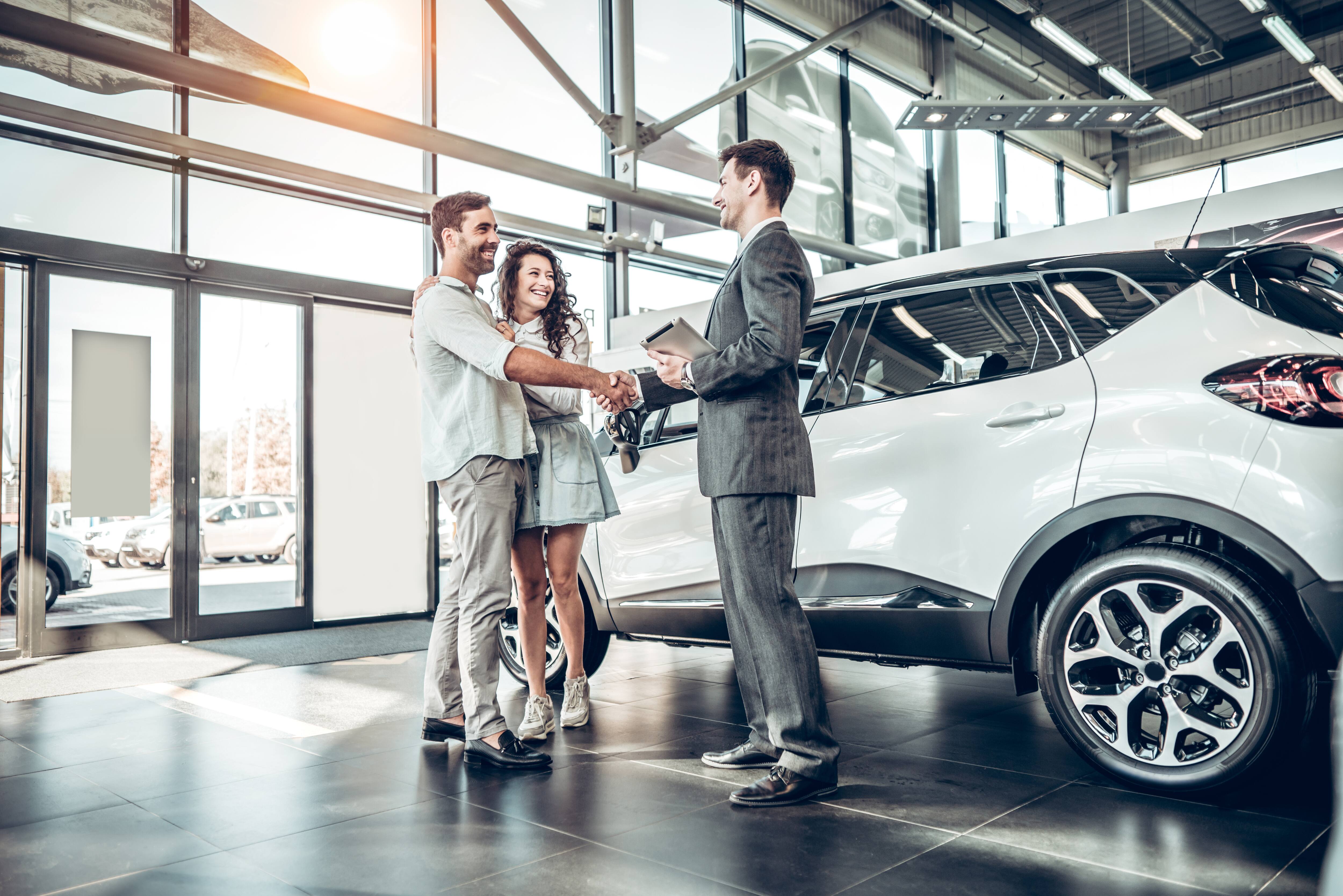 young couple shaking hands with car sales agent