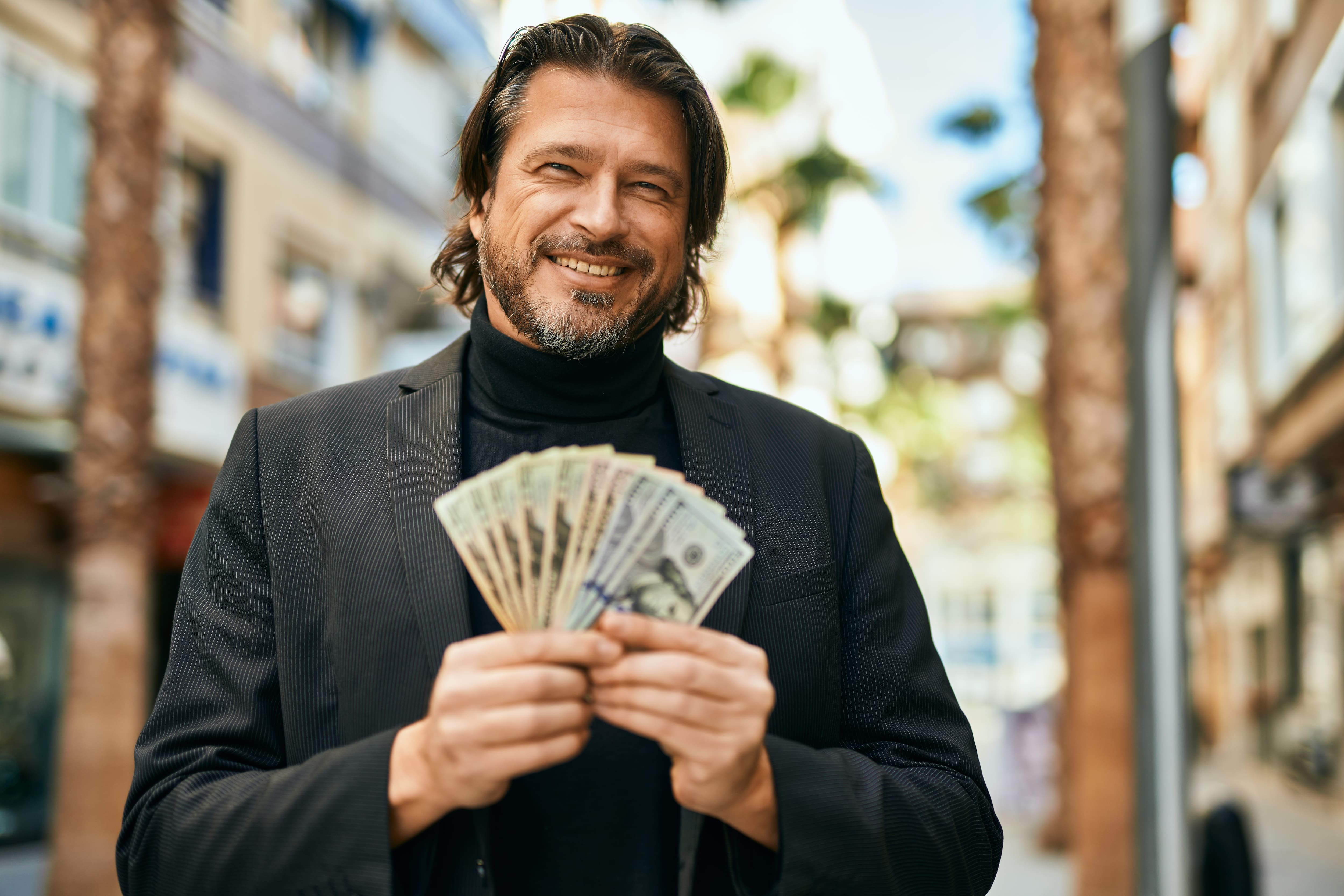 businessman smiling holding dollars at the city.