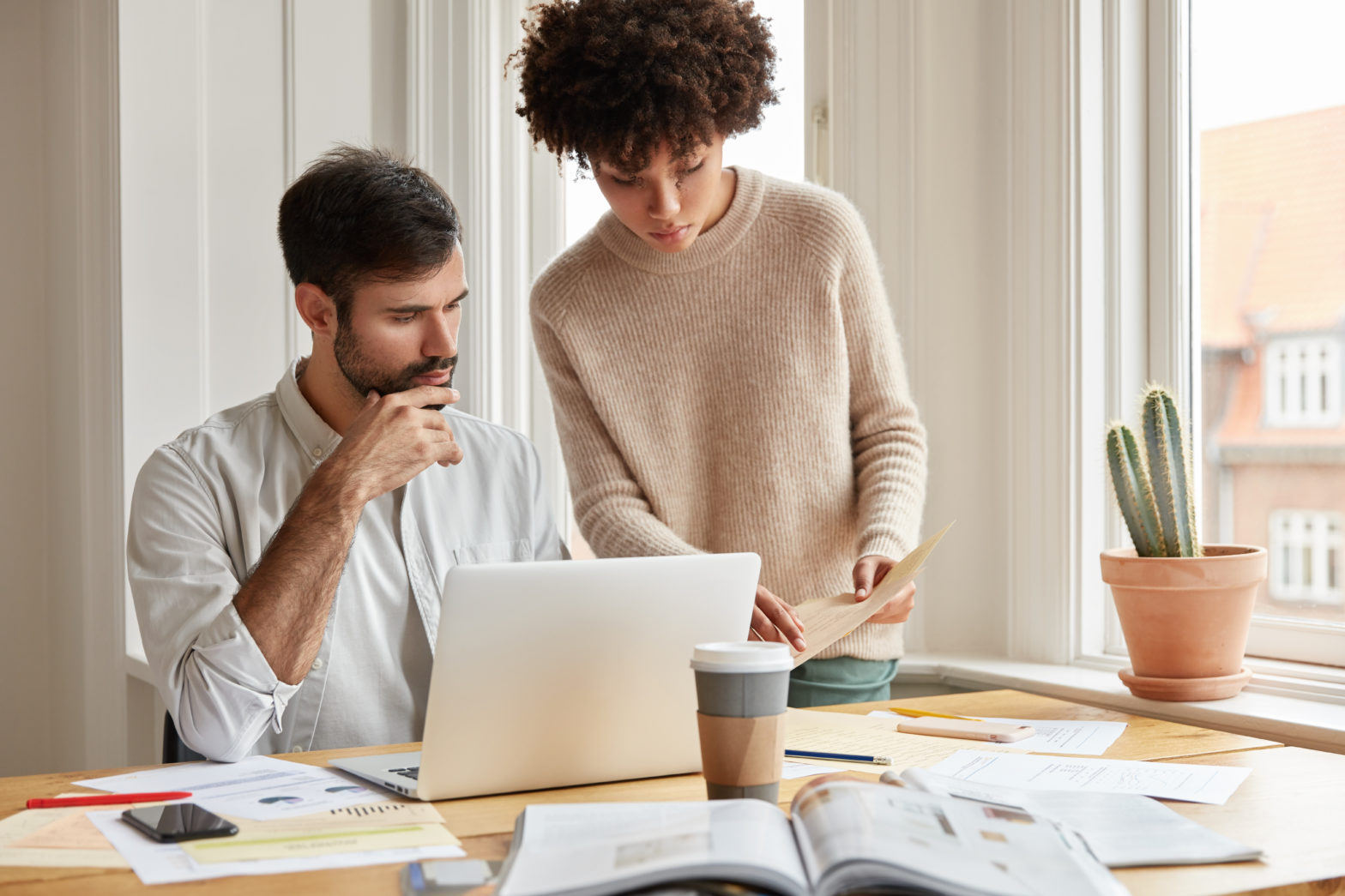 Young women showing inflation document to a man sitting at desk in front of laptop