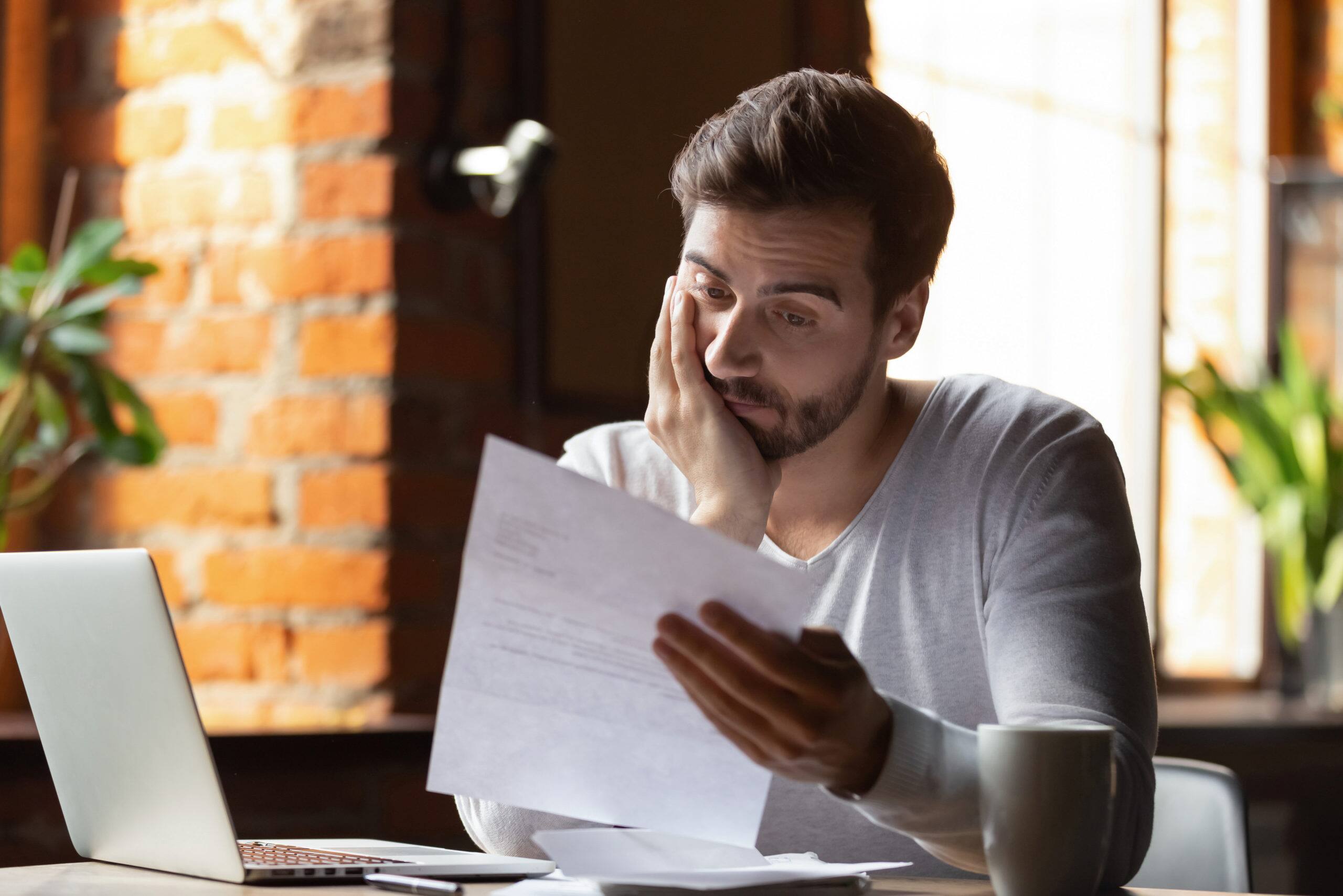 Confused frustrated young man reading CD taxes and interest in cafe