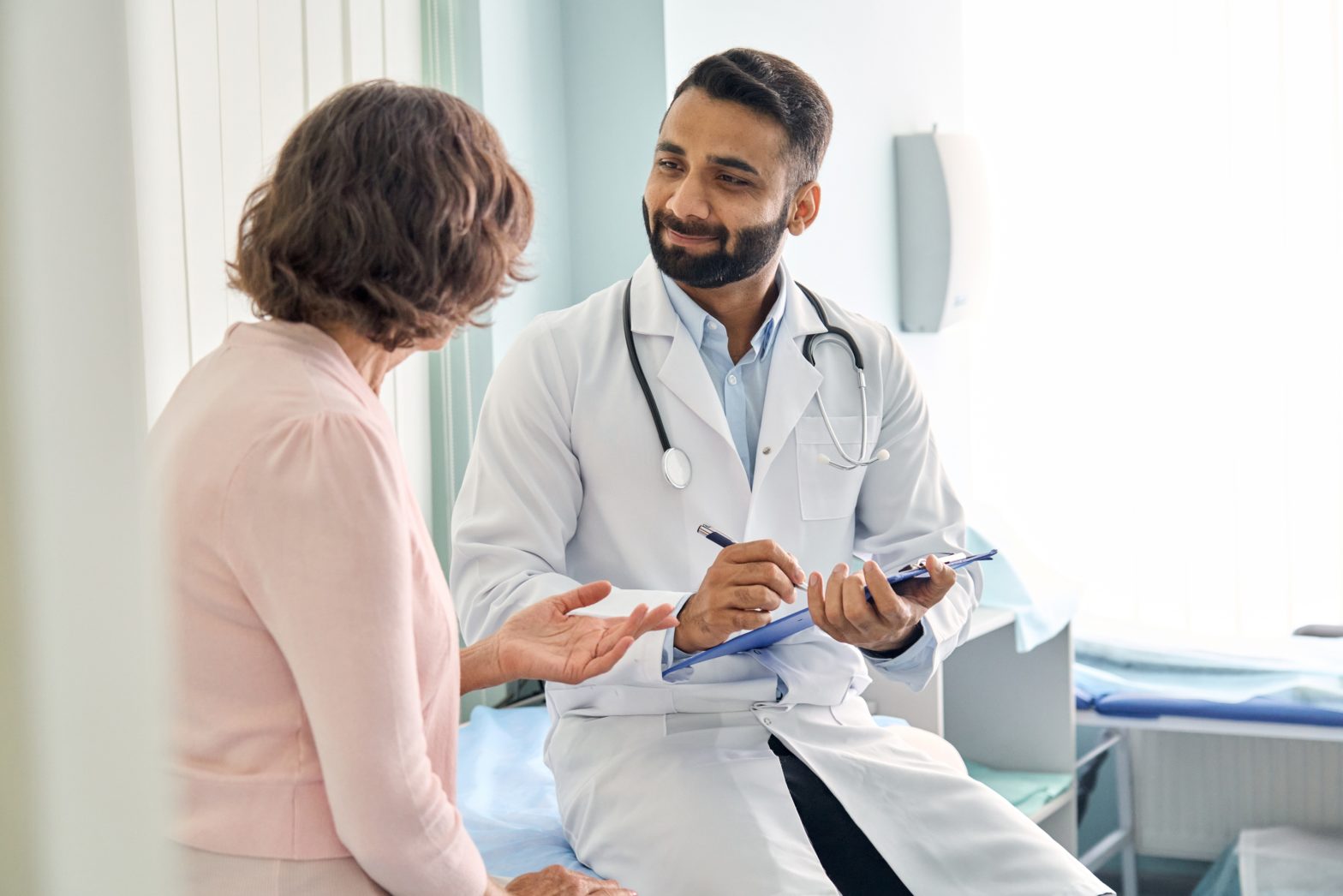 Indian male doctor consulting to senior old female patient and filling form