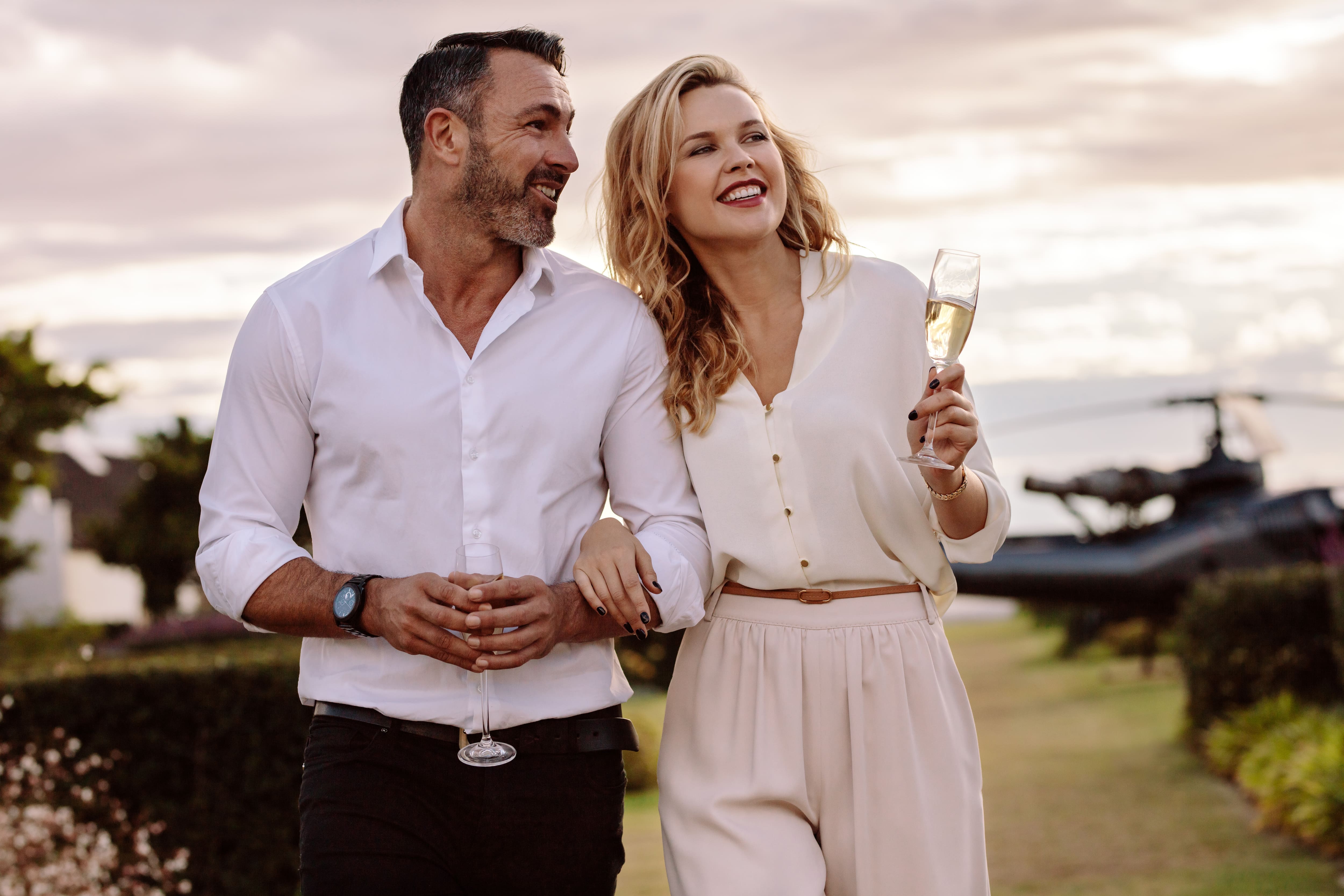 Rich couple walking together outdoors holding wine glass