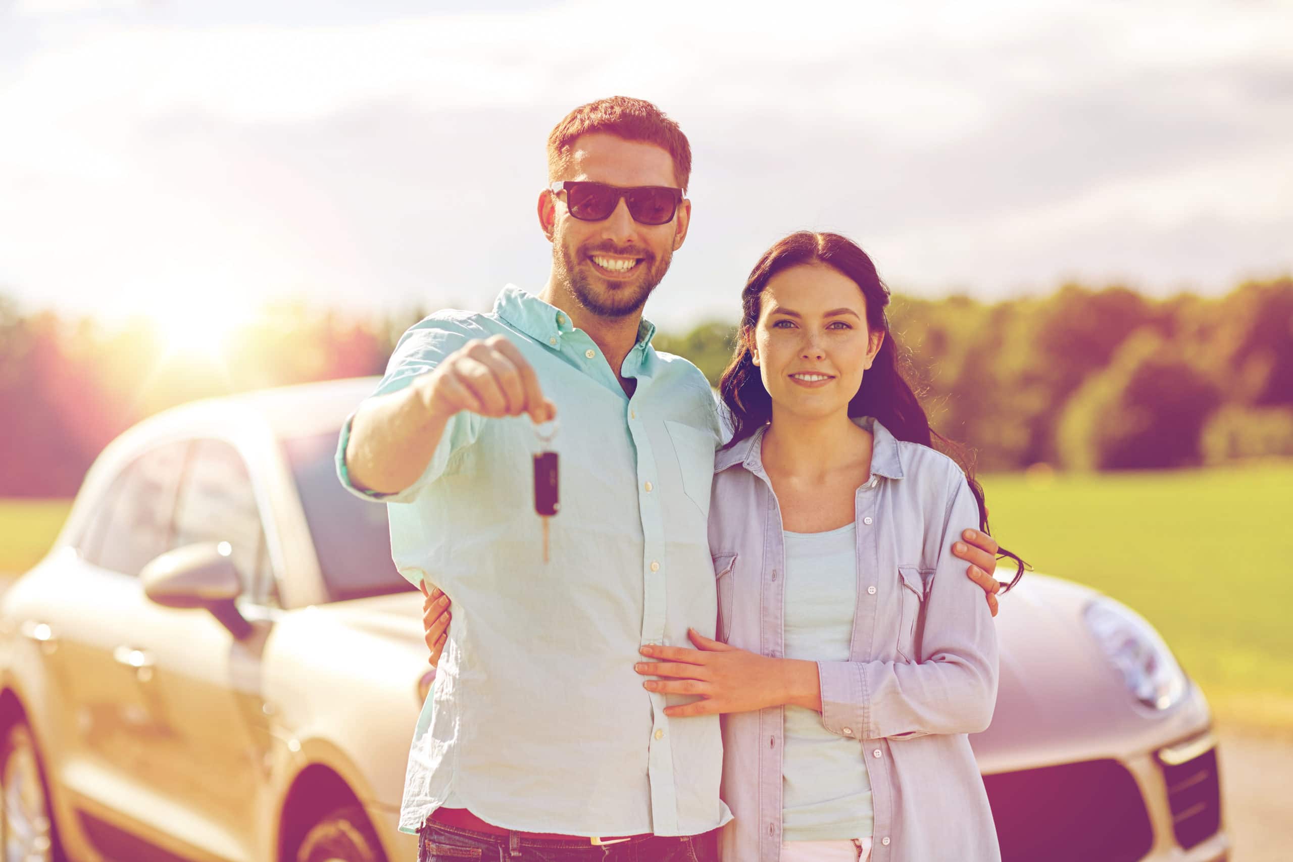 couple showing car key with car on road trip