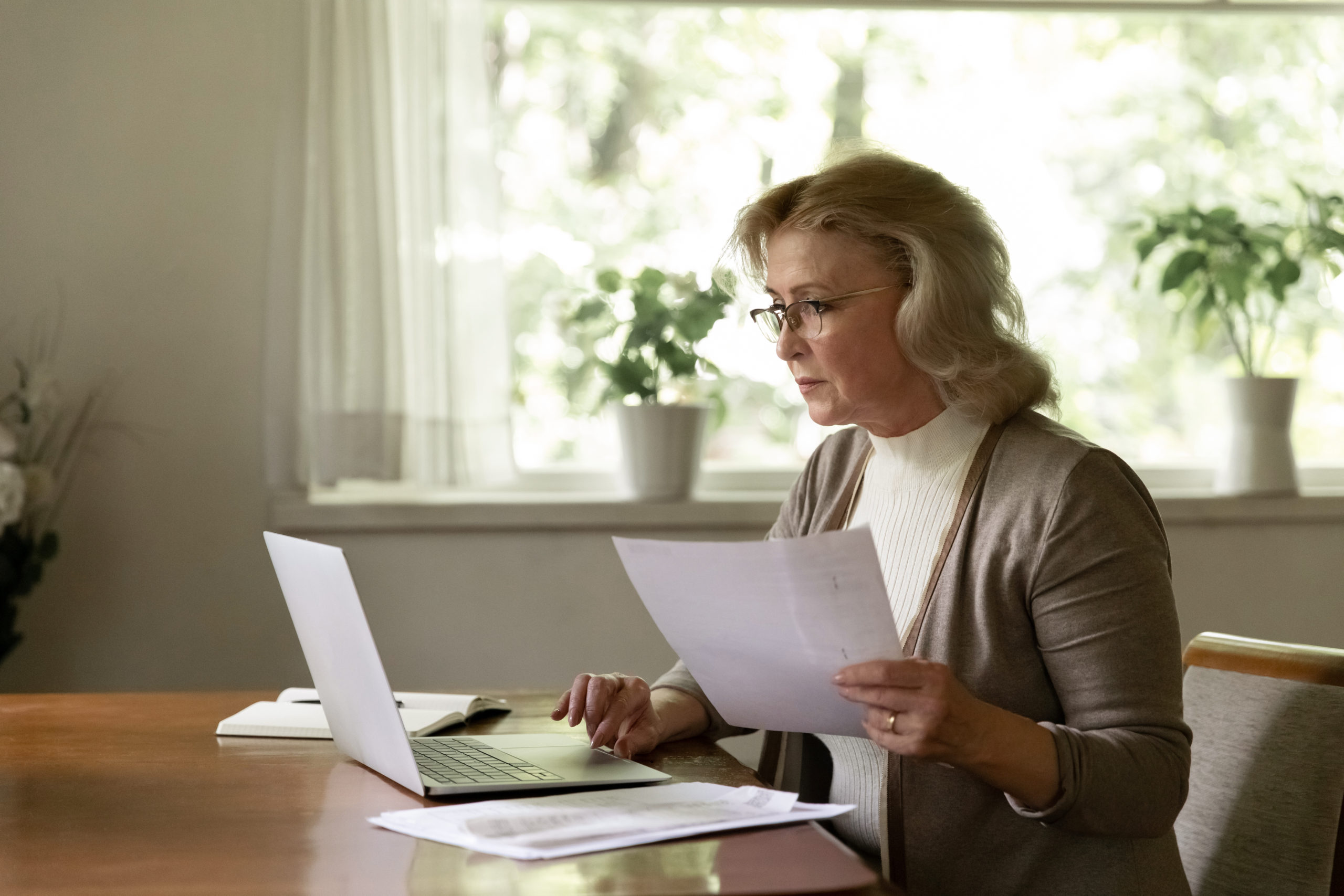 woman holding document and using laptop