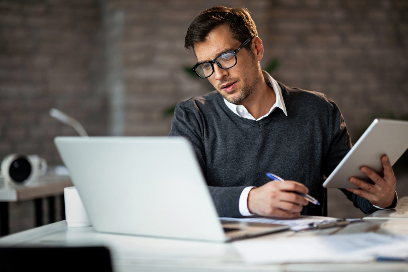 Man using touchpad looking at laptop and writing to decide to borrow for investing or not