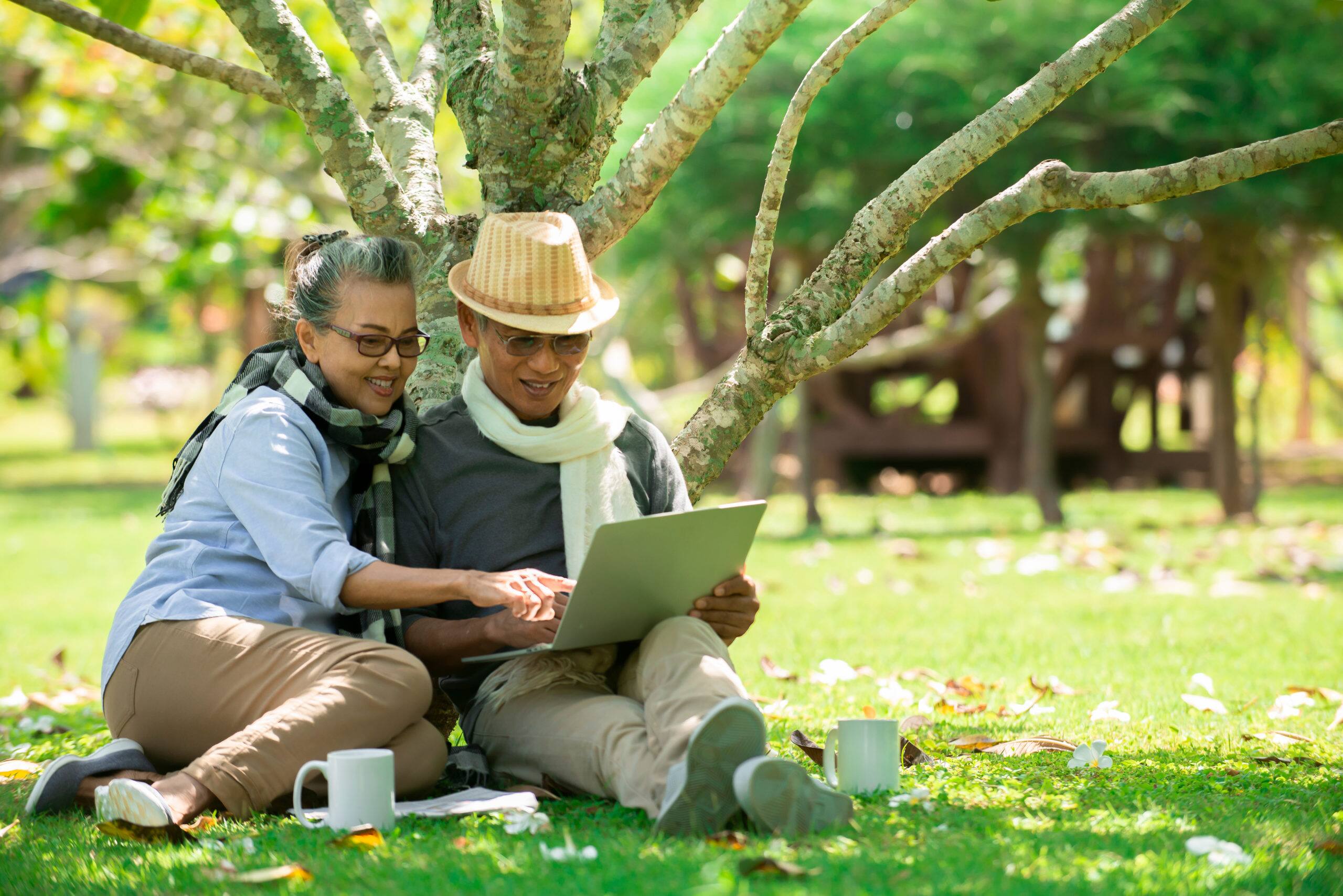 senior couple sitting at park while using laptop