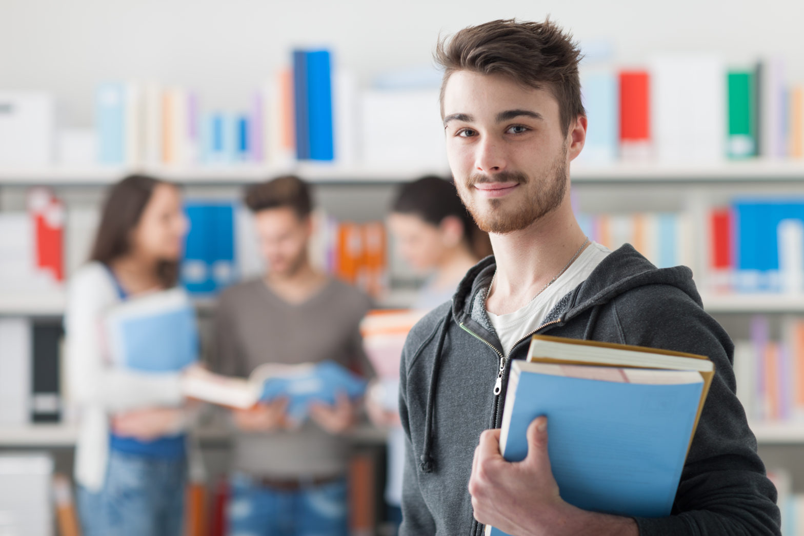 confident handsome student holding books and smiling