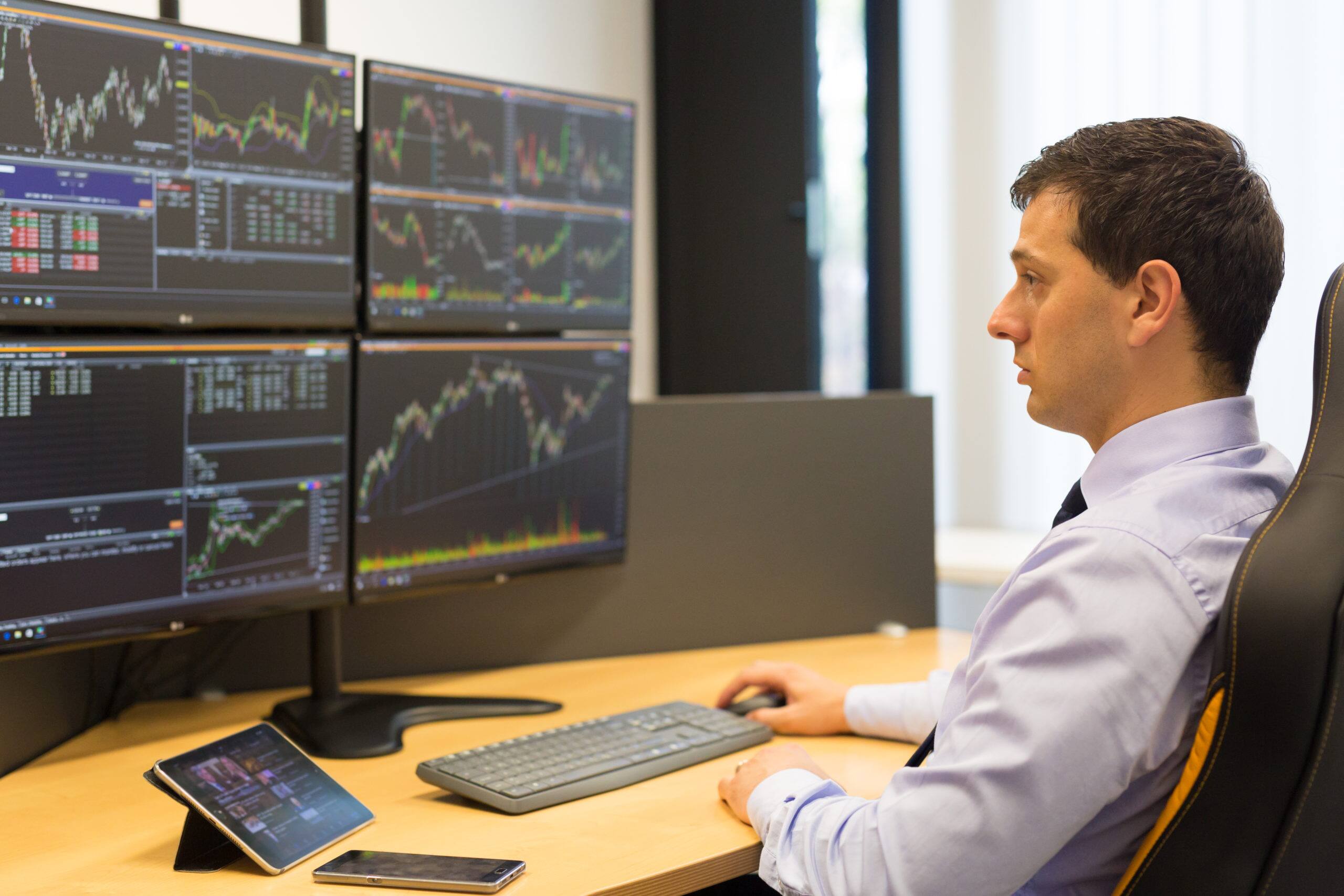 trader sitting in front of four computer screen and working on bonds