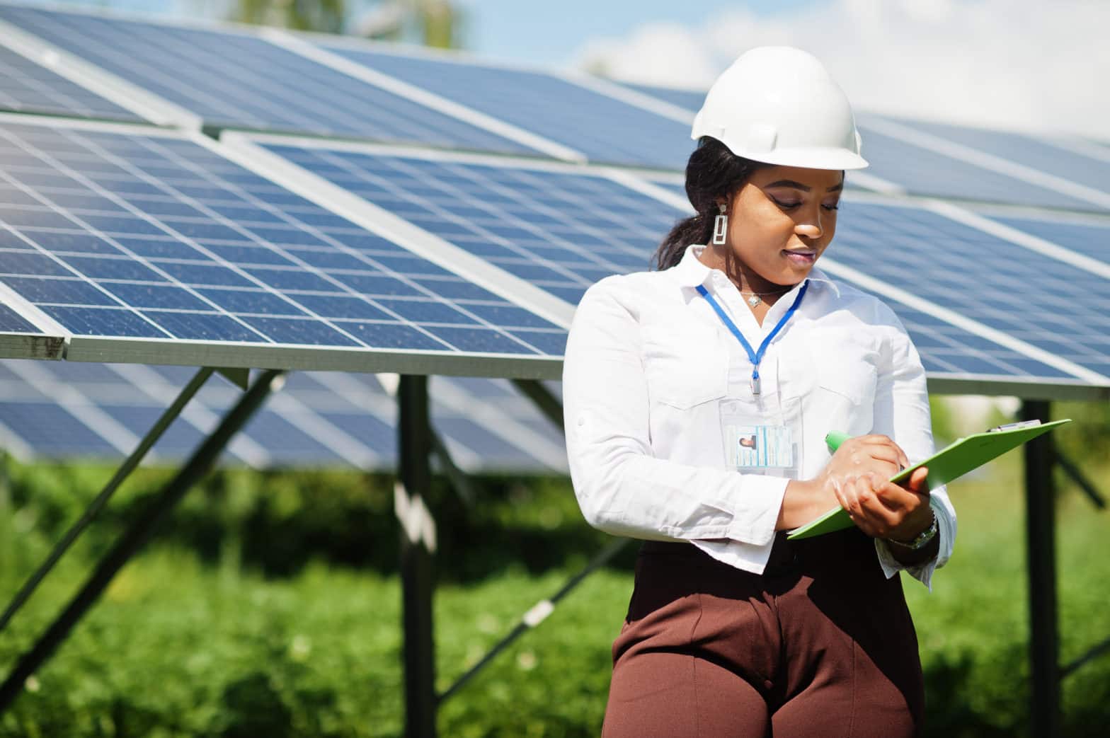 A female worker standing in front of solar panels writing on a notepad