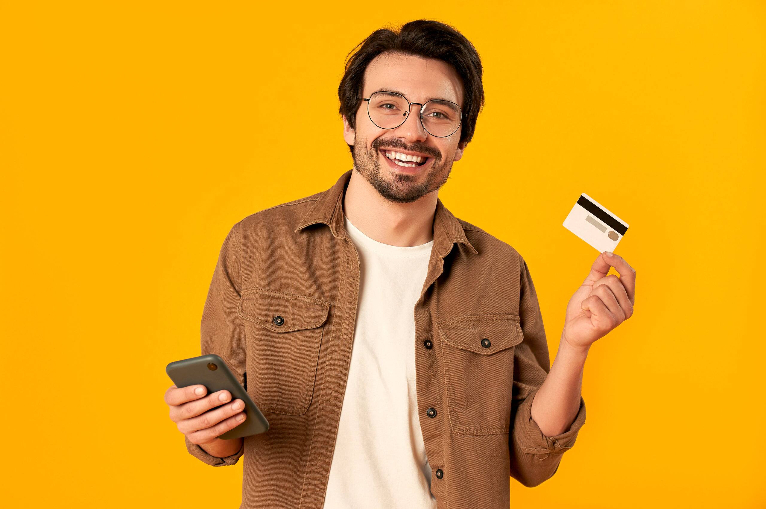 man in glasses holds credit card and smartphone