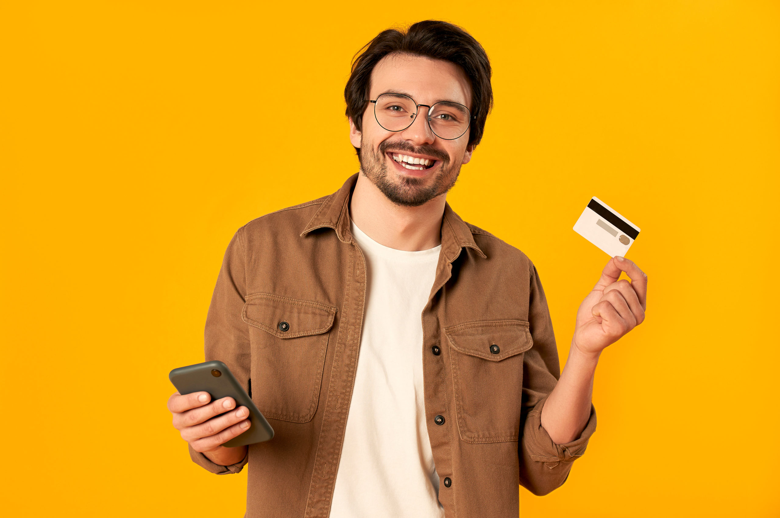 man in glasses holds credit card and smartphone