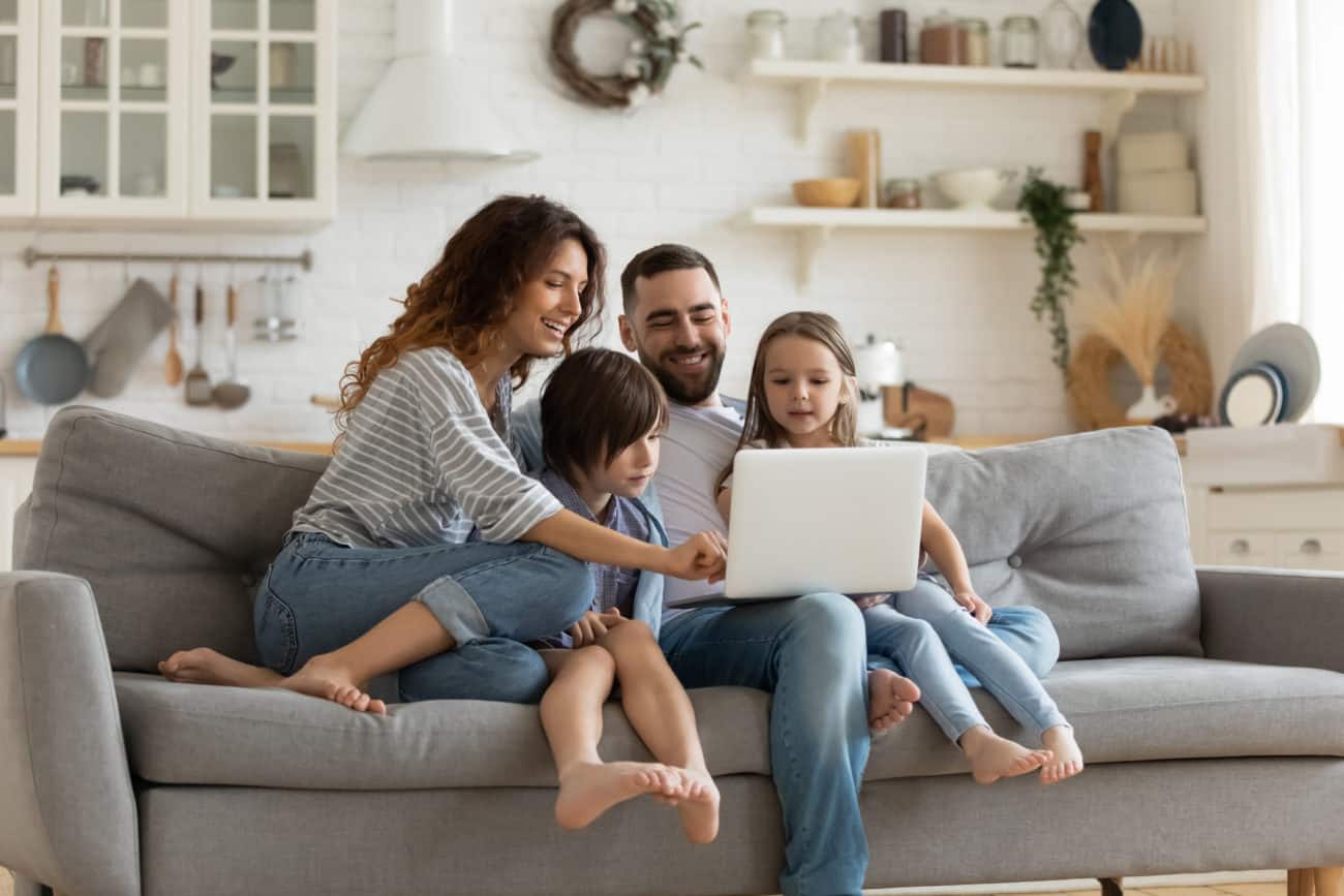 A family sits on a couch and uses a computer together