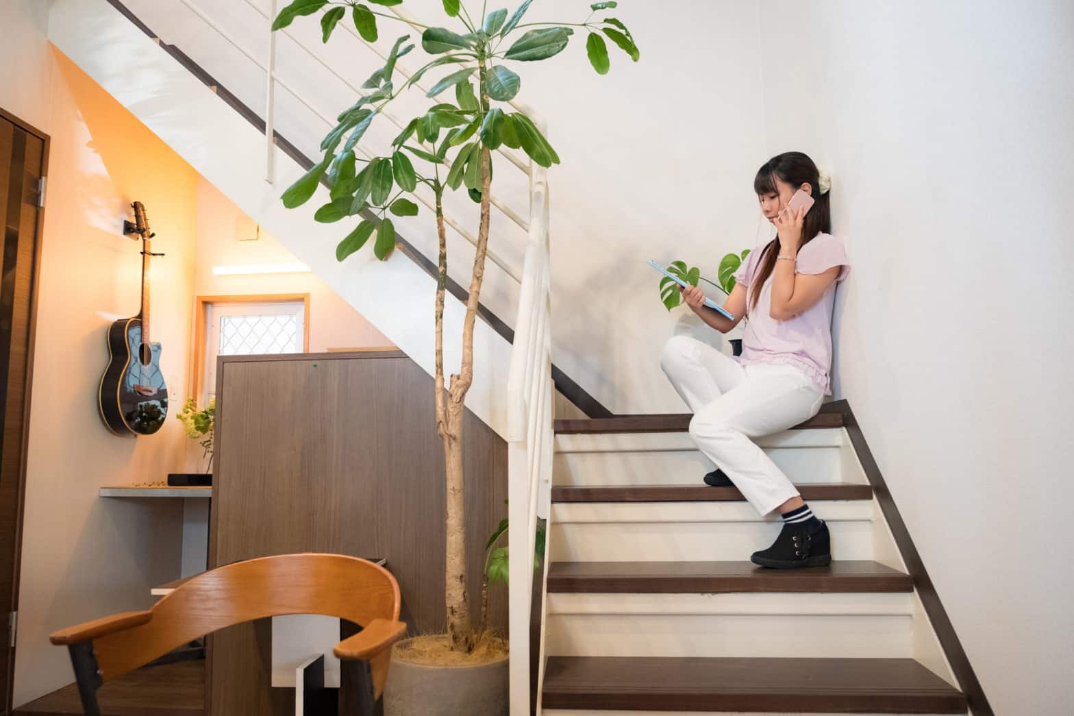 A woman talks on her phone and looks on her laptop as she sits on the stairs of her modern office