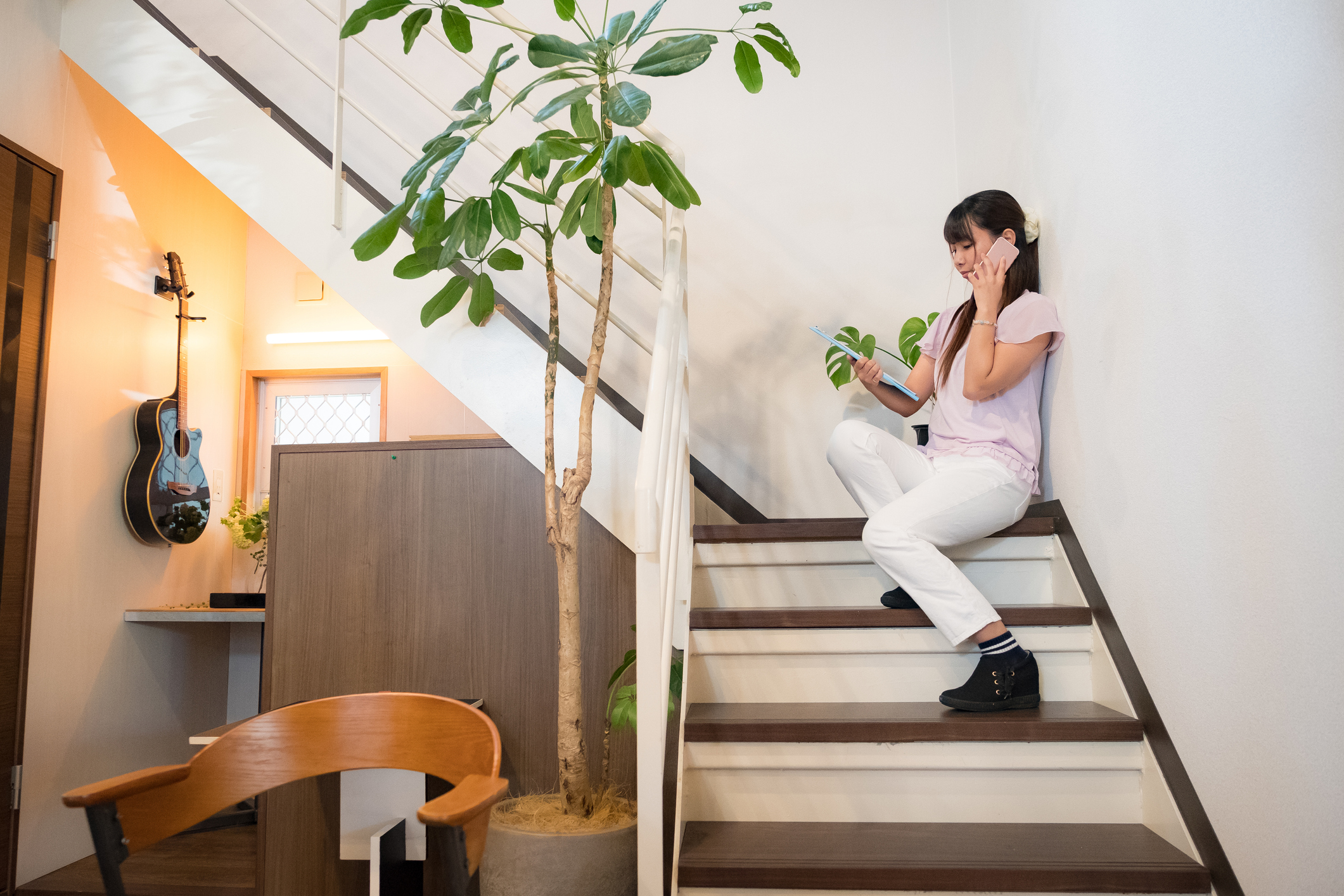 A woman talks on her phone and looks on her laptop as she sits on the stairs of her modern office