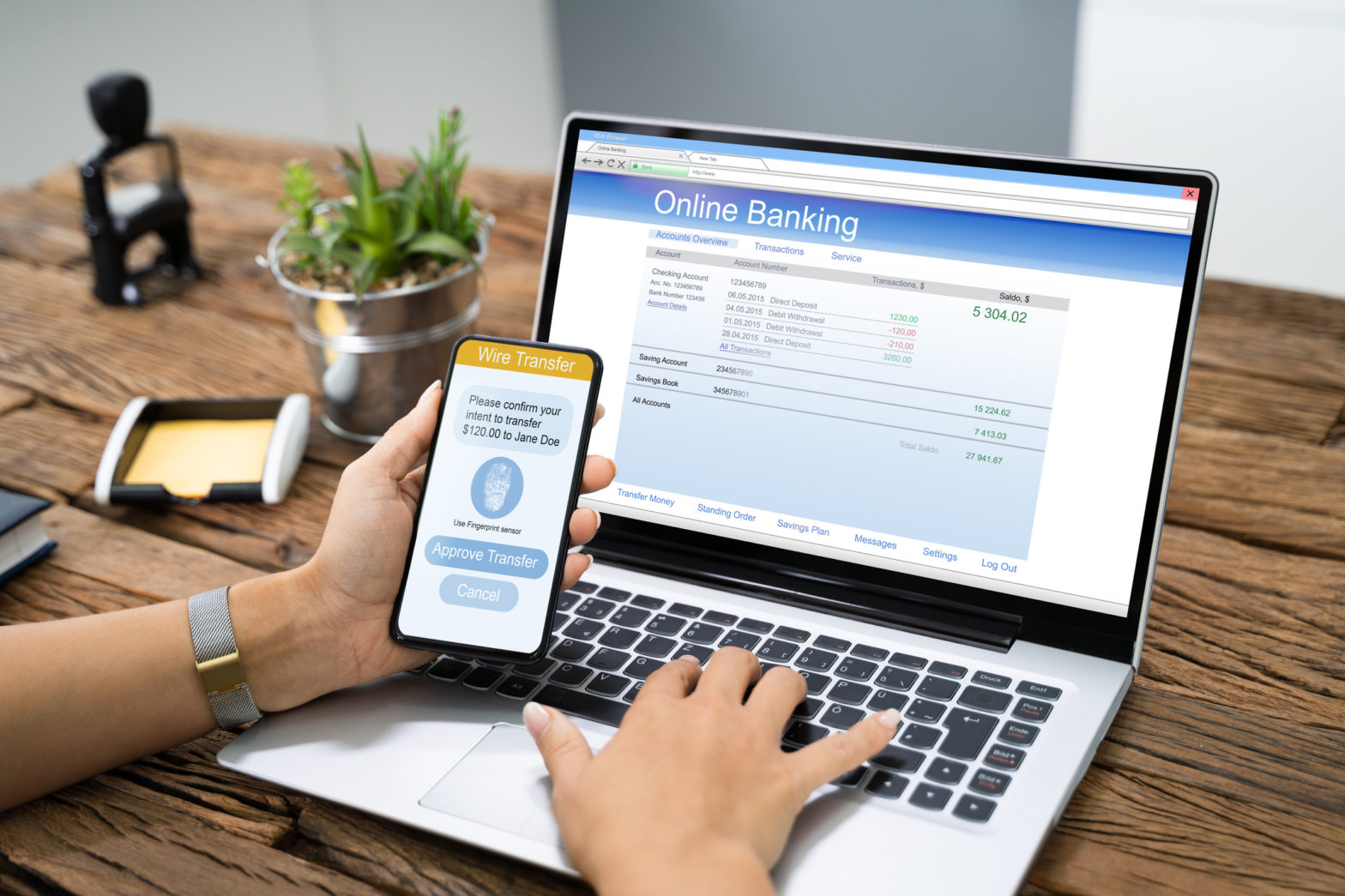 Hands hold a mobile phone while working on a laptop to do online banking