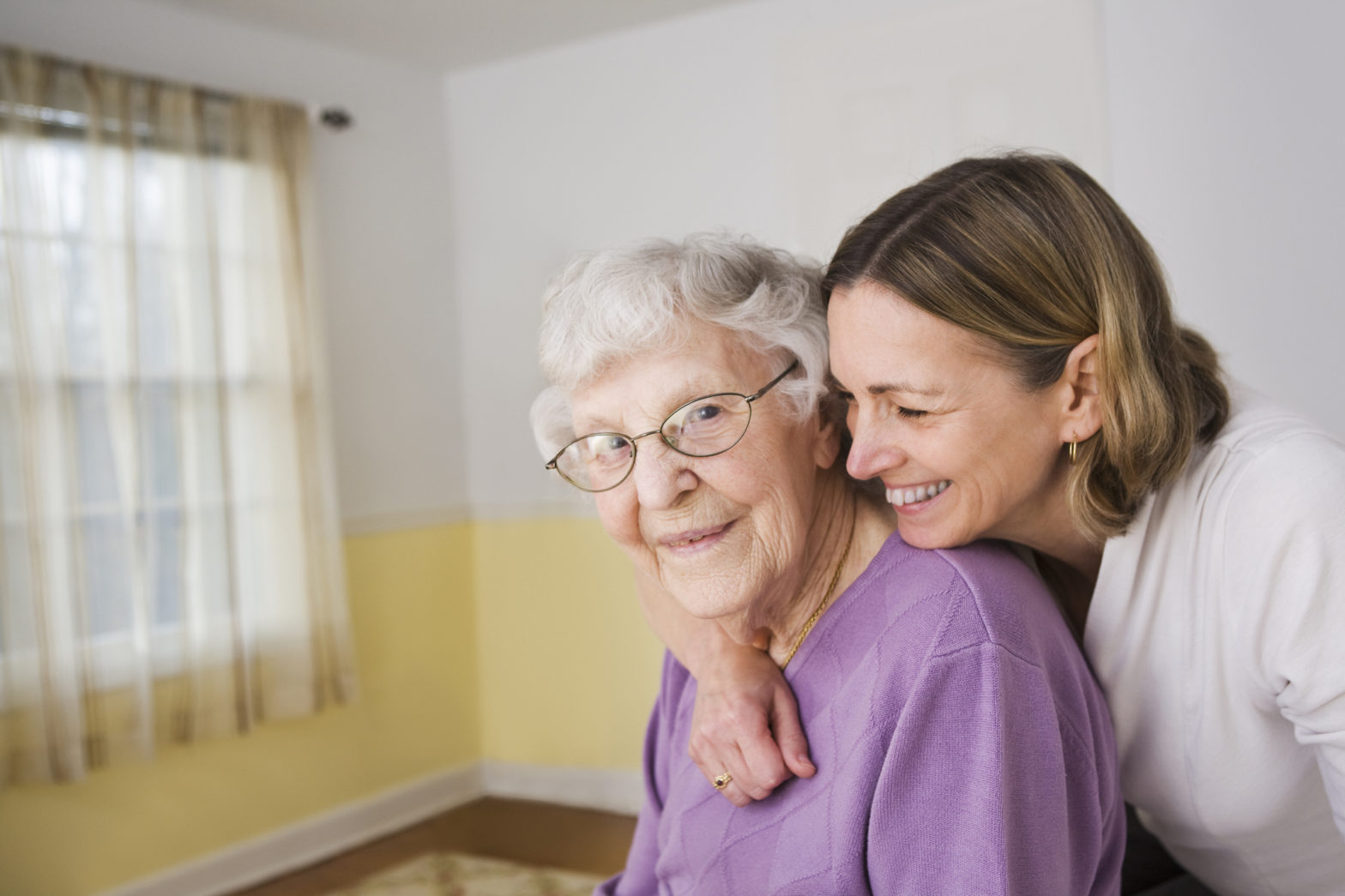 A young woman is hugging an older lady from behind