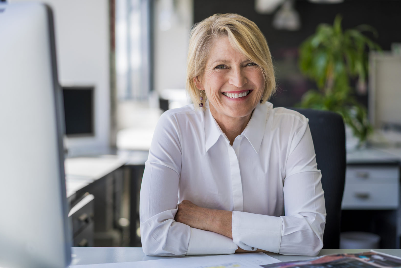 A woman sits at a desk in the workplace smiling