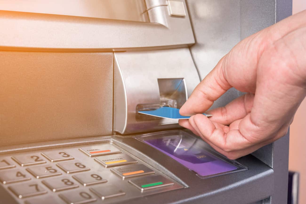 A man's hand can be seen using an ATM with his bank card