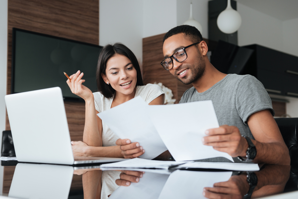 A young couple consider their mortgage options as they review paperwork and look at a computer