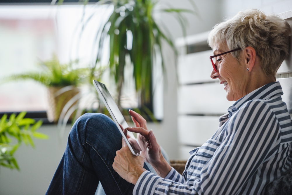 A woman sits on the floor of her kitchen while she looks at her tablet