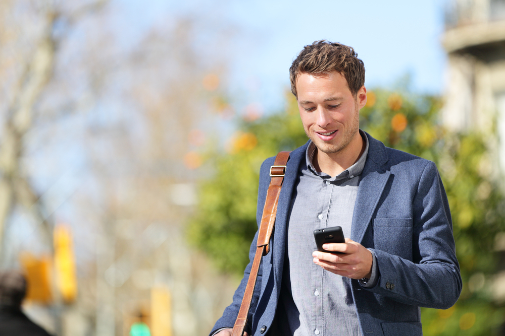 A young man checks his money market balance on his mobile phone while he is walking outside