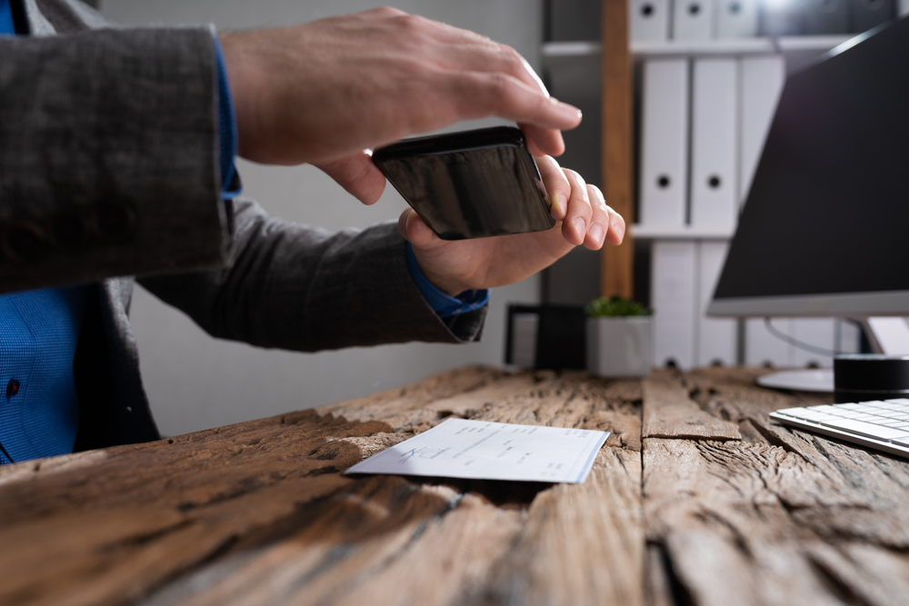 A person holds his phone over a paper check in order to deposit through his bank's mobile app