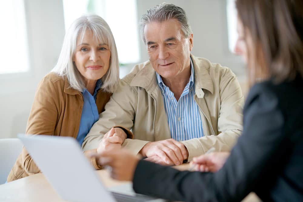A retired couple discuss their retirement money situation with a financial advisor while they all look at a computer as the advisor shows them their account online