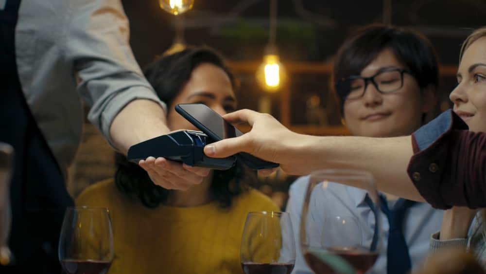 A young person uses his phone to pay for dinner in a restaurant with his friends