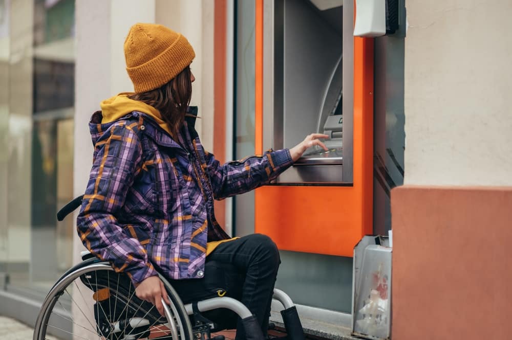 A woman who uses a wheelchair is using an ATM to deposit money into her savings account