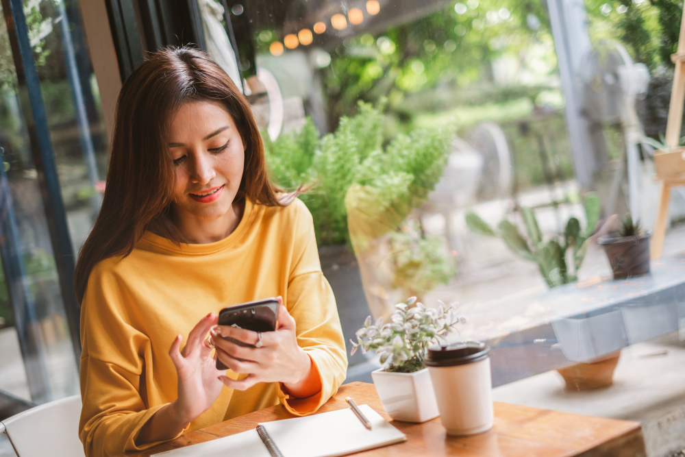 a woman in a cafe is sitting at a table with a notebook in front of her as she looks at her phone