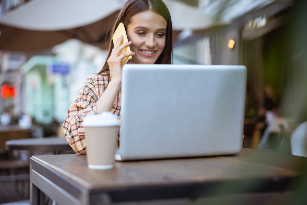 A young woman uses her laptop computer at an outdoor cafe to do her banking.