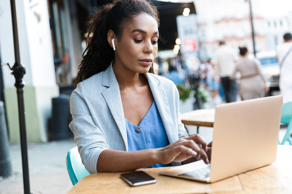 A young woman works on her computer at an outdoor cafe