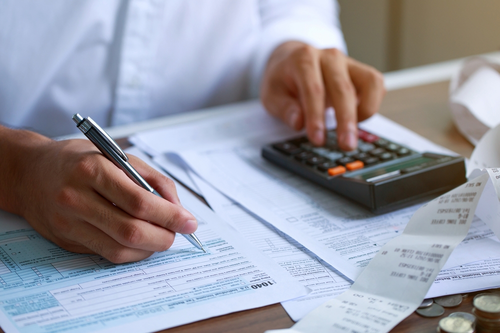 A man's hands can be seen preparing his federal tax return at the last minute