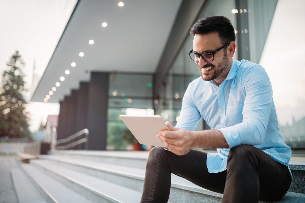 A man sits outside as he looks at his CD purchase on his tablet.