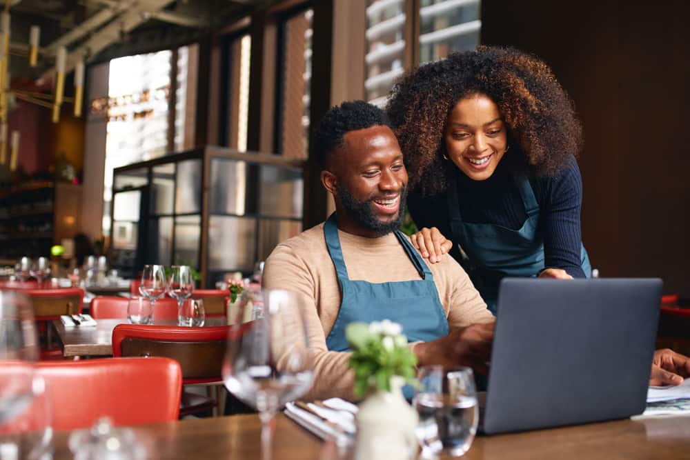 Small business owners sit in their restaurant using laptop for banking