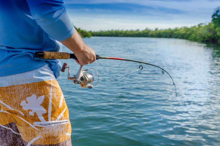 A man enjoys his early retirement with a day of fishing. He is holding a fishing pole and standing on the banks of a river.